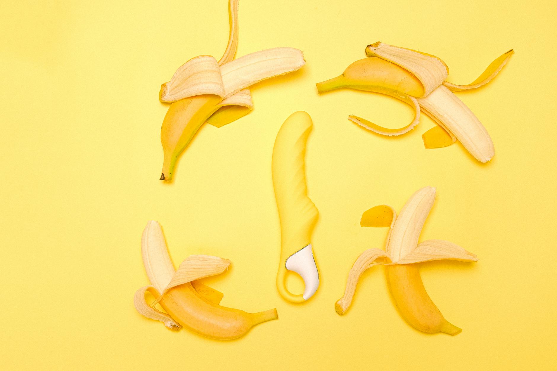 A yellow silicone lemon vibrator surrounded by peeled lemons on a bright yellow background.