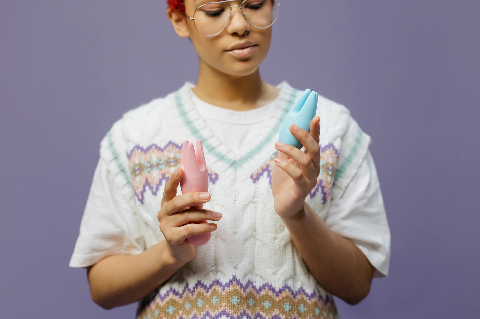 Woman holding blue and pink silicone vibrators in a thoughtful, contemplative moment.