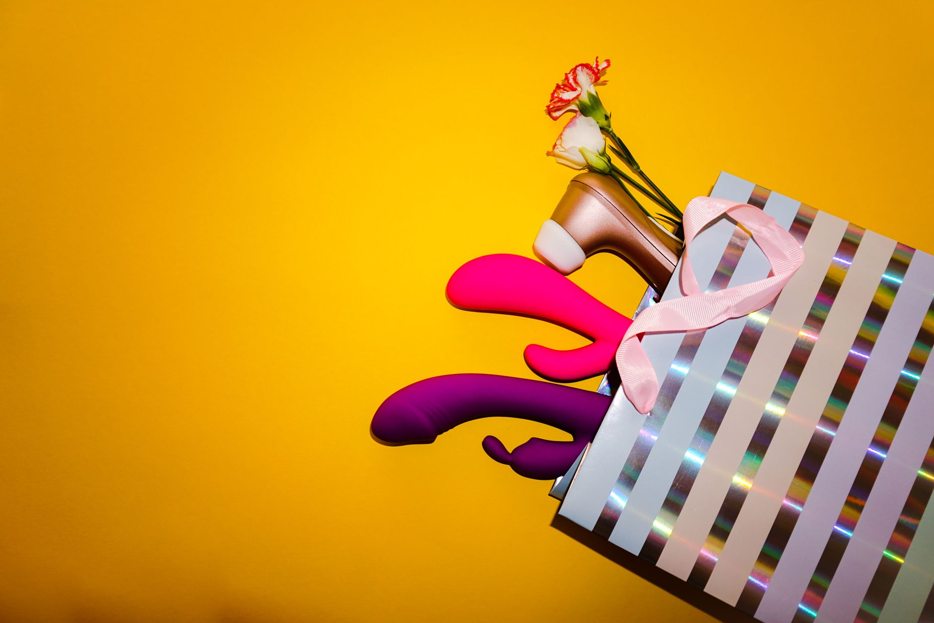 Colorful lemon vibrators and flowers in a holographic gift bag against a bold yellow background