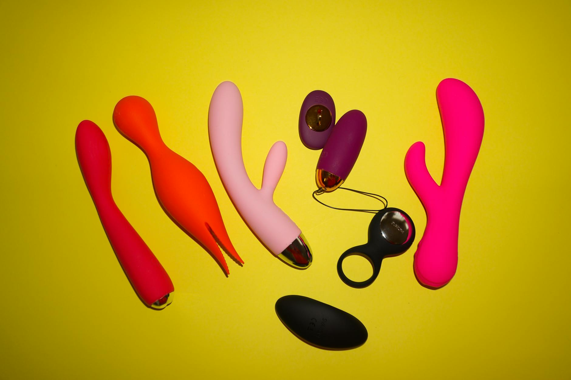Studio display of colorful clitoral vibrators including Lemon Suction toys on bright yellow background