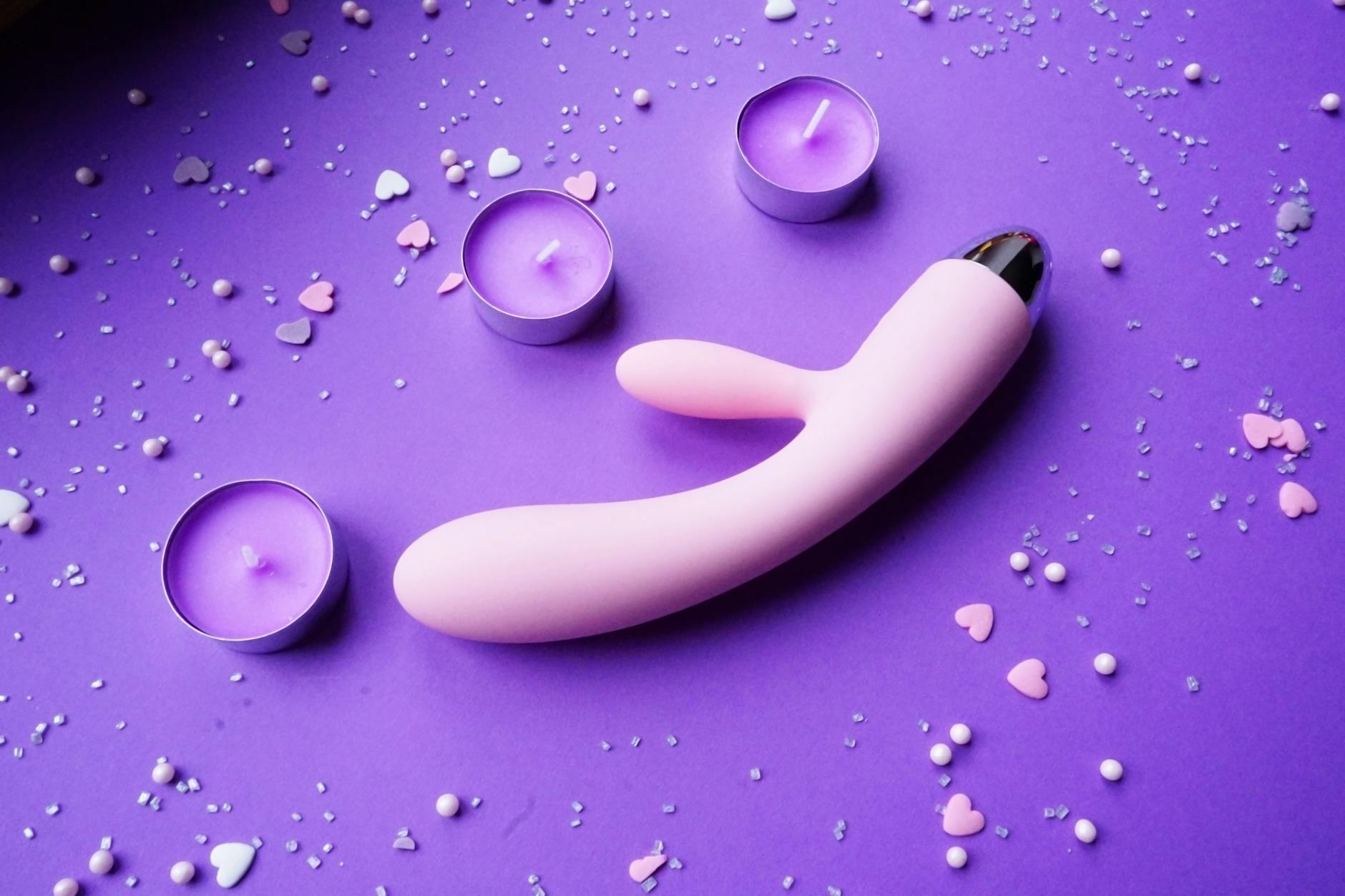A soft pink vibrator surrounded by heart confetti and candles, symbolizing gentle self-care and rebuilding intimacy.